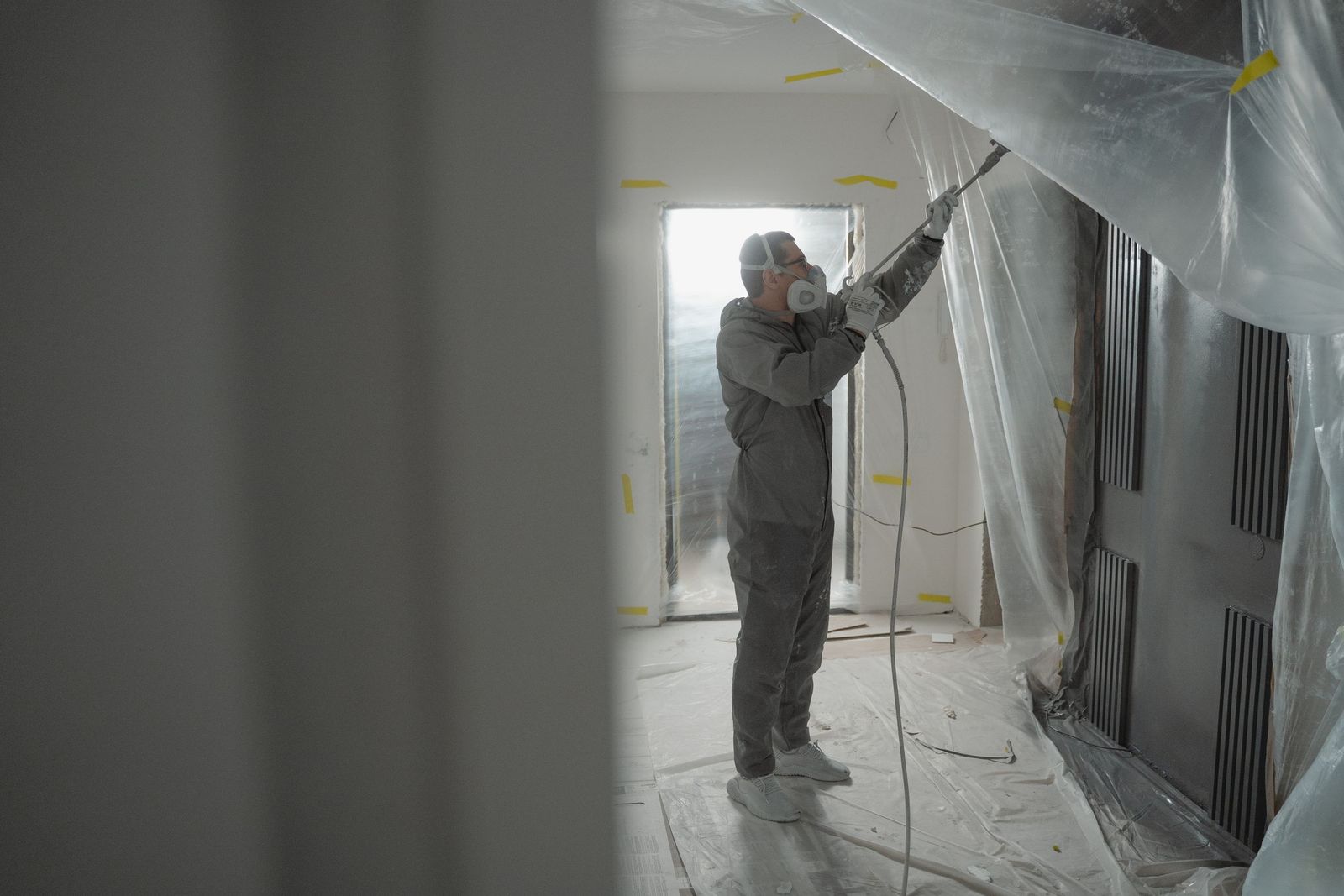 Technicien masqué traitant une pièce confinée sous bâches plastiques