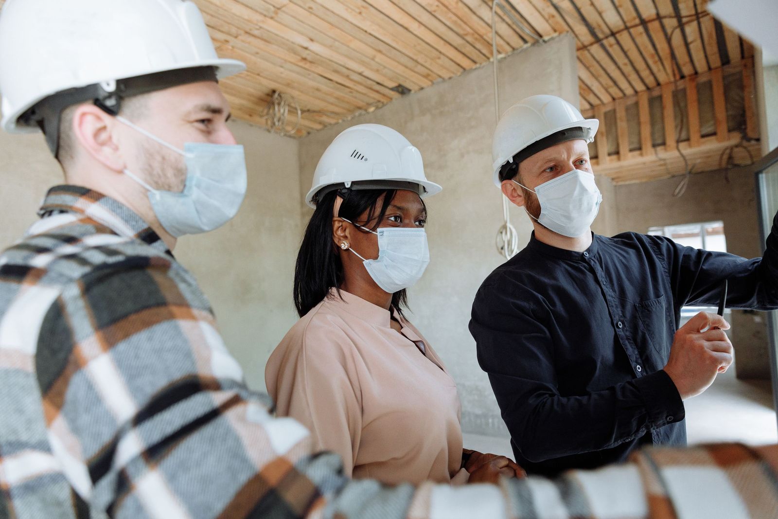 Trois professionnels casqués et masqués faisant le point dans un local en travaux