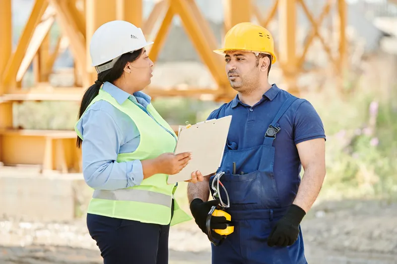 Responsable de chantier en gilet de sécurité faisant le point avec un ouvrier, porte-bloc en main