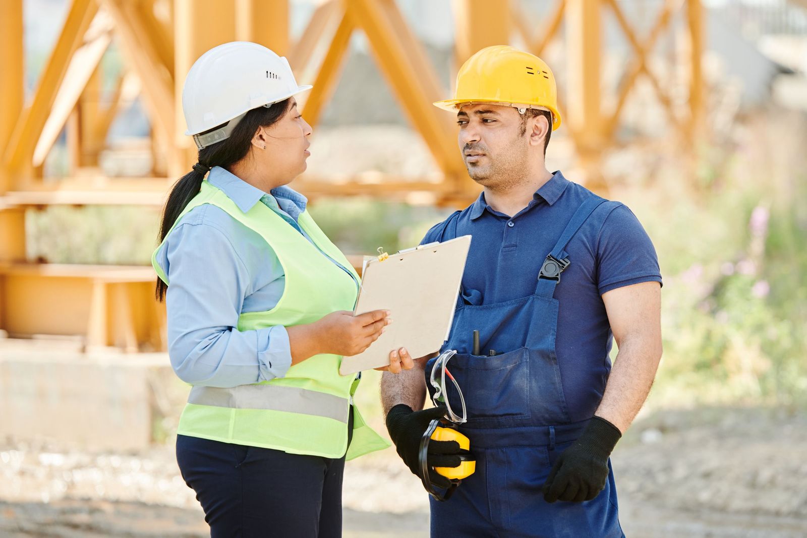 Responsable de chantier en gilet de sécurité faisant le point avec un ouvrier, porte-bloc en main