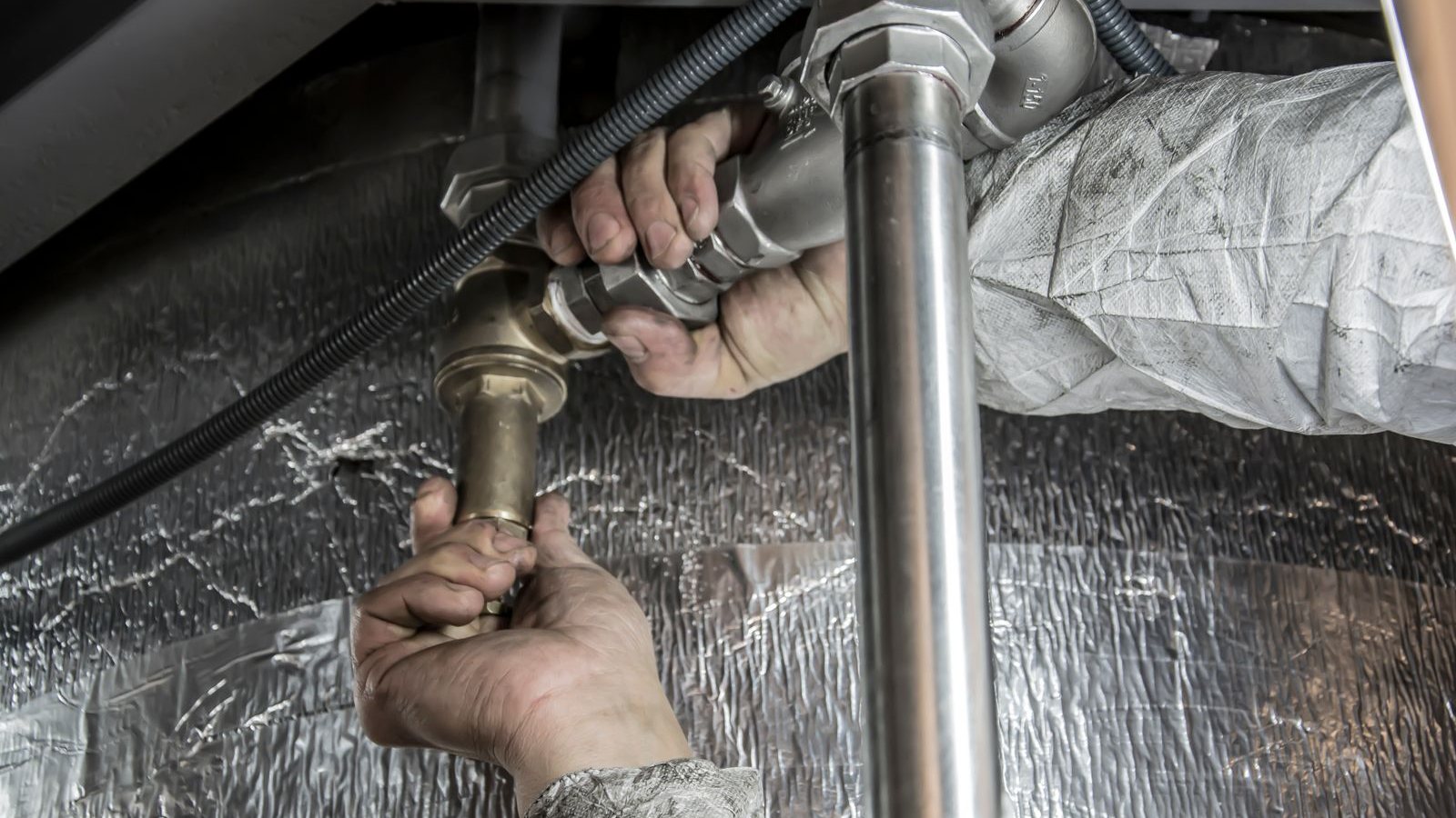 Mains d'un plombier sur une canalisation qui fuit