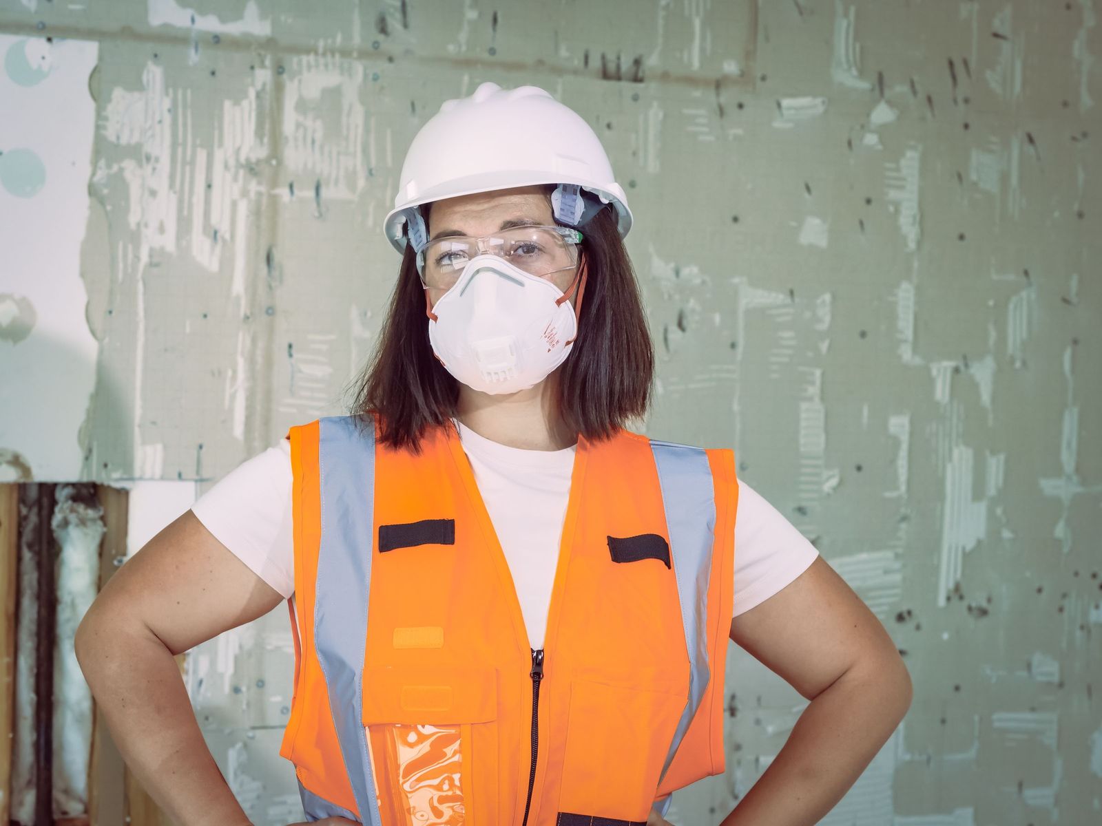 Technicienne en casque, gilet et masque de protection sur un chantier de rénovation