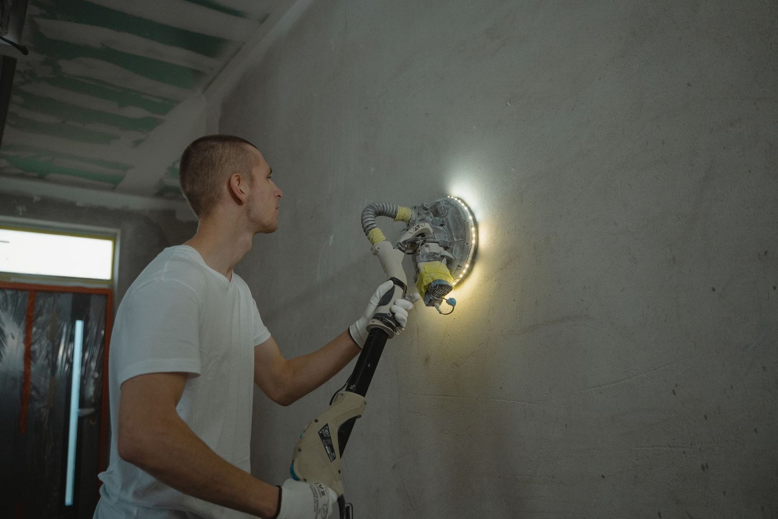 Plaquiste ponçant un mur à la ponceuse girafe avant les finitions
